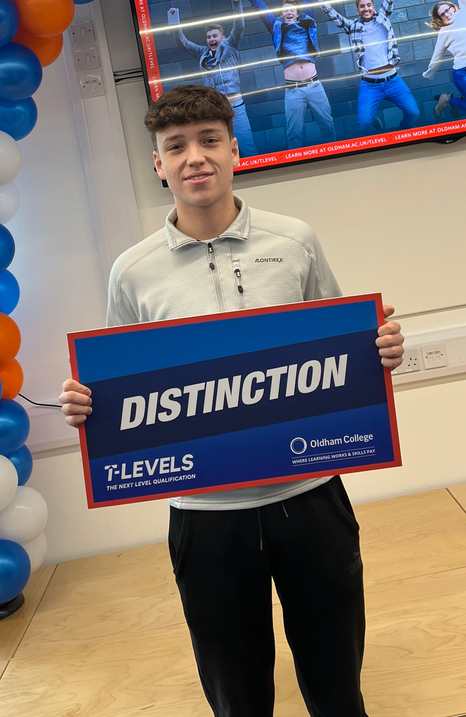 Male T Level Student Holding up a large crd reading Distinction