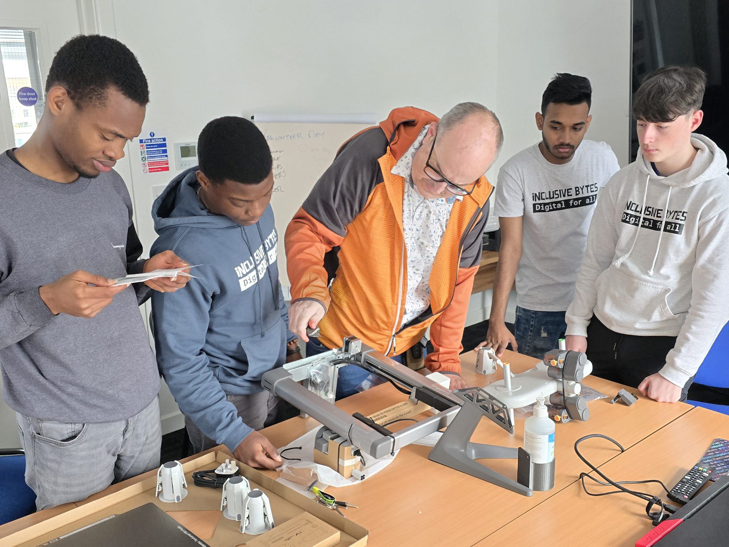 Five people crowd around digital equipment laid on a table.