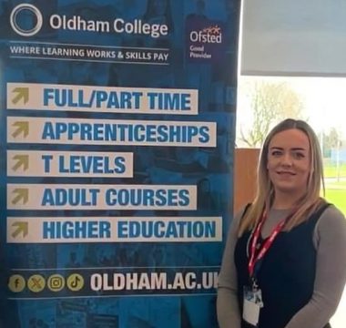 Courtney stands next to an Oldham College banner.