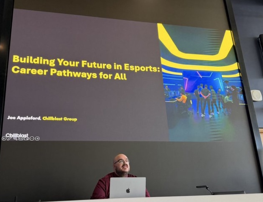 A person sitting at a laptop, beneath a screen which reads Your Future in Esports: Pathways for All.