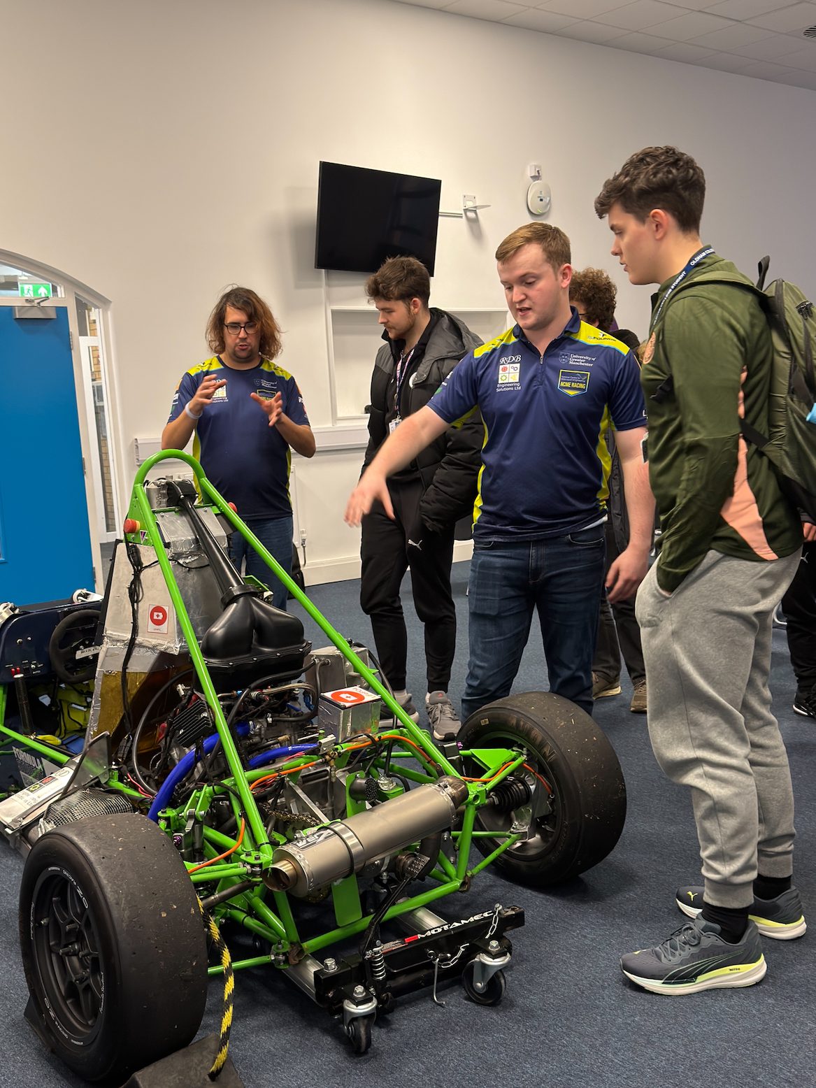 A group of people looking at a small formula 1 car.