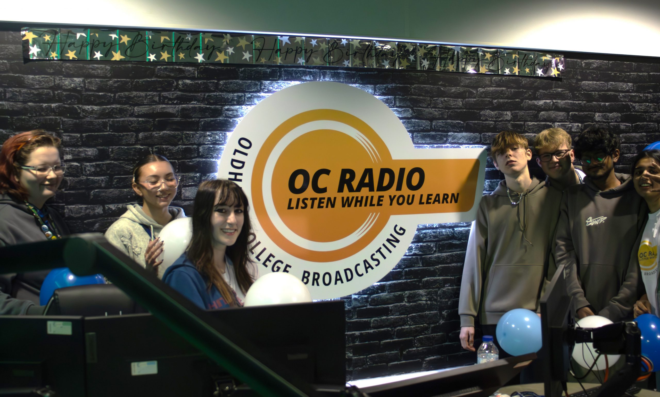 Group photo of students next to the OC Radio sign.