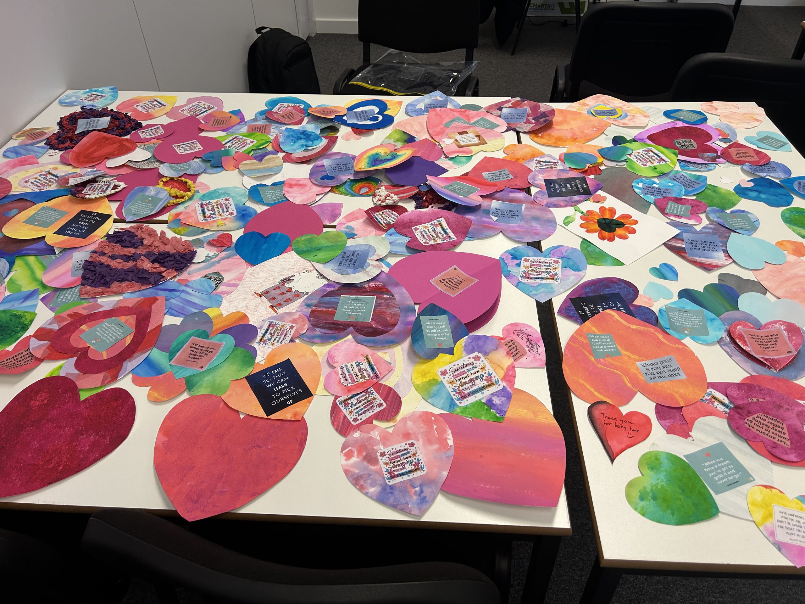 Paper hearts in assorted colours are laid on a table. Some have typed notes attached to them.