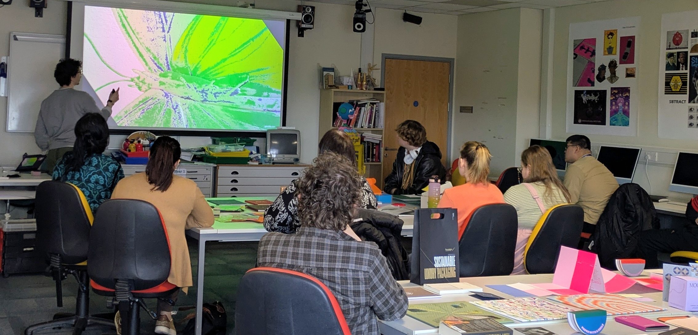 A classroom of students watch someone deliver a presentation.