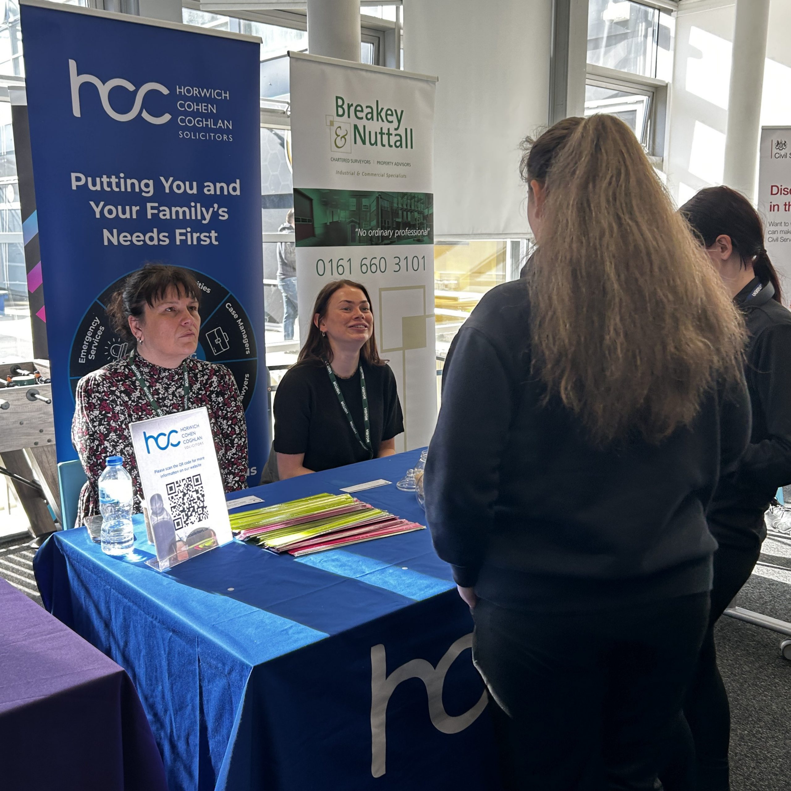 Two people sit behind an information stand, looking at two people standing
