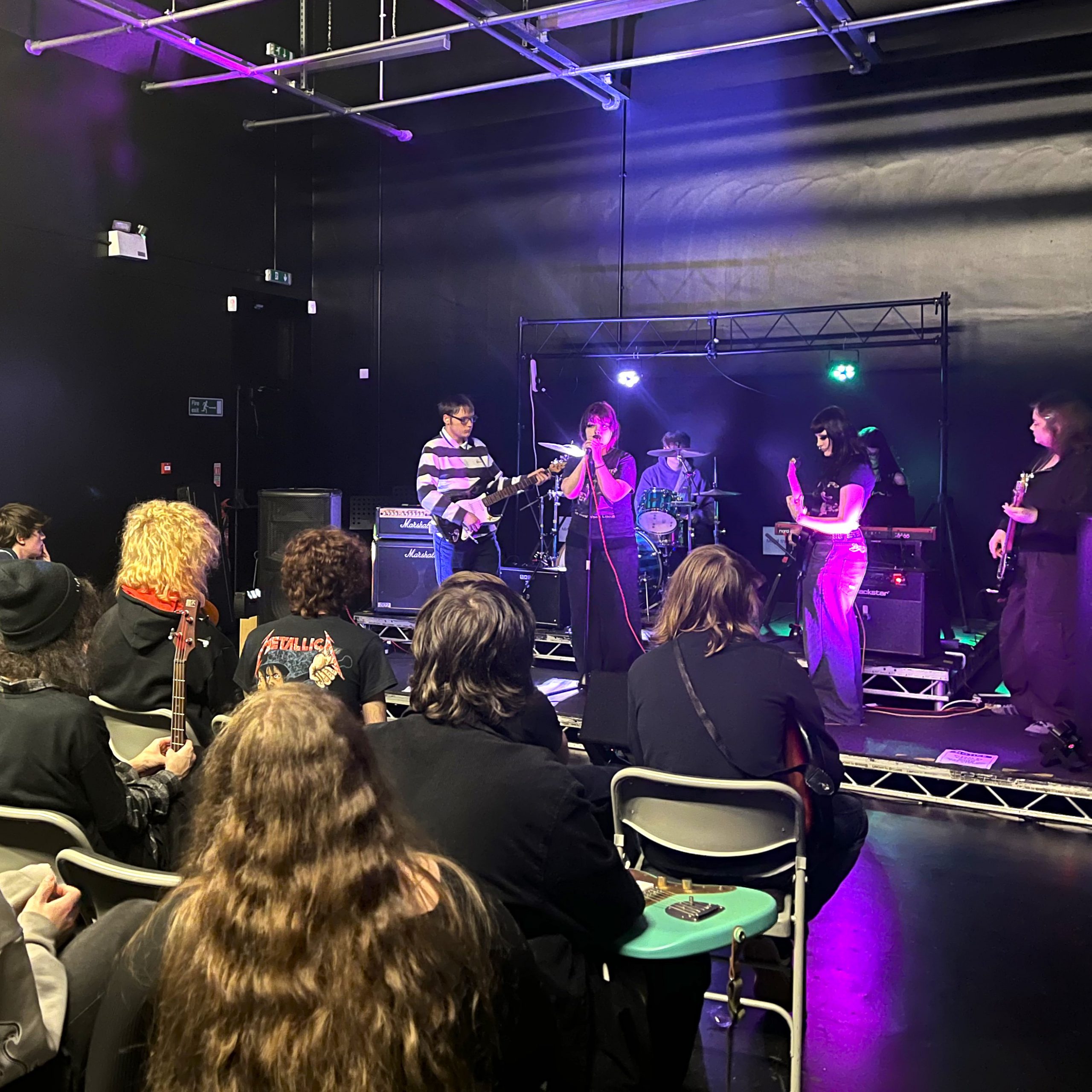A band stand on a stage in front of an audience and play musical instruments 