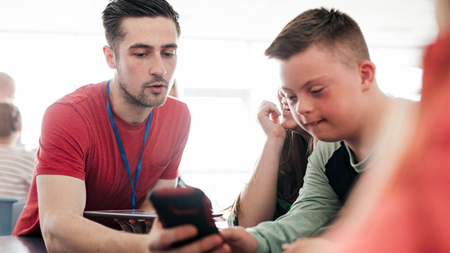 A male tutor supports a young student with Downs Syndrome