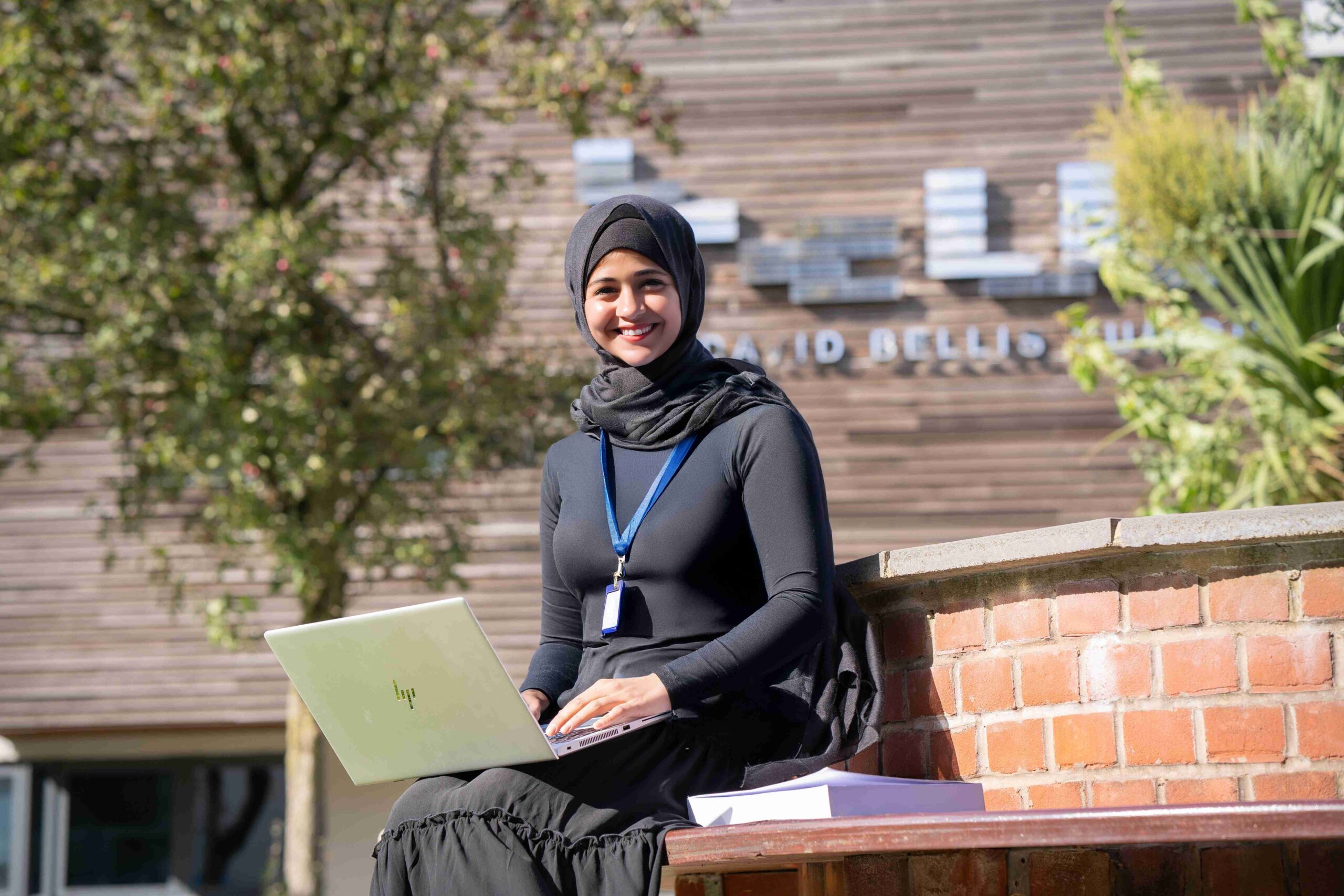 Female college student sat with a laptop on her knee outside