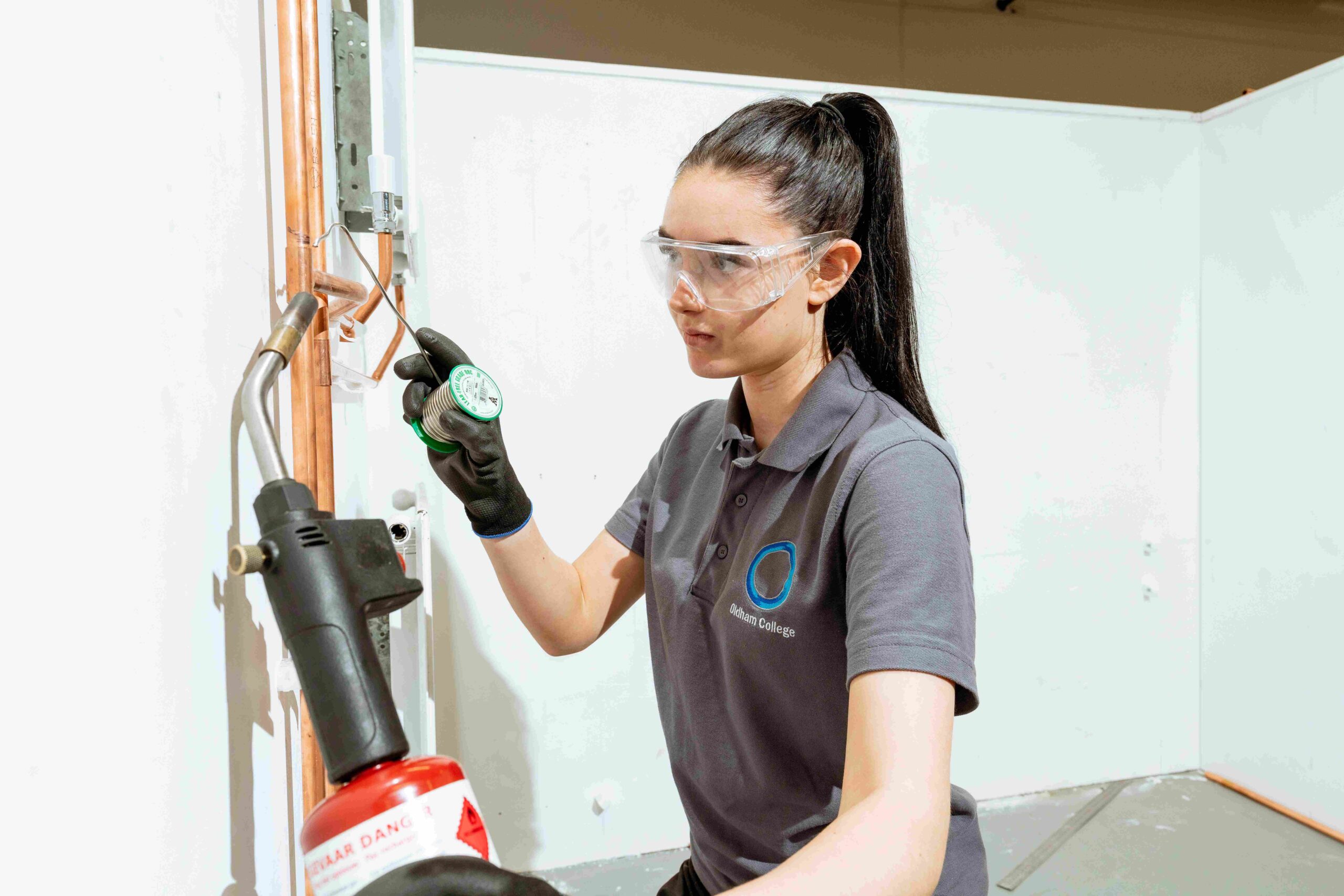 Female plumbing apprentice welding a pipe in college workshop