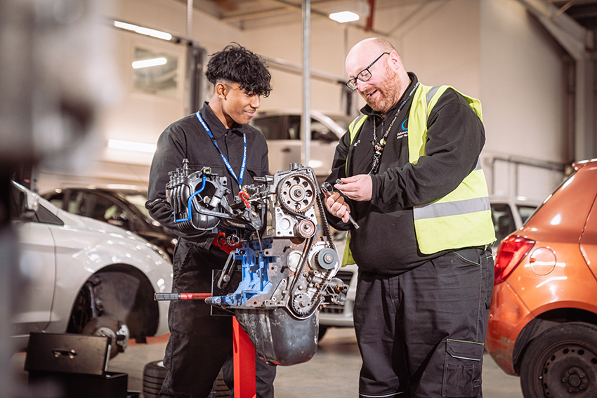 A male automotive student stood with a male tutor working with tools