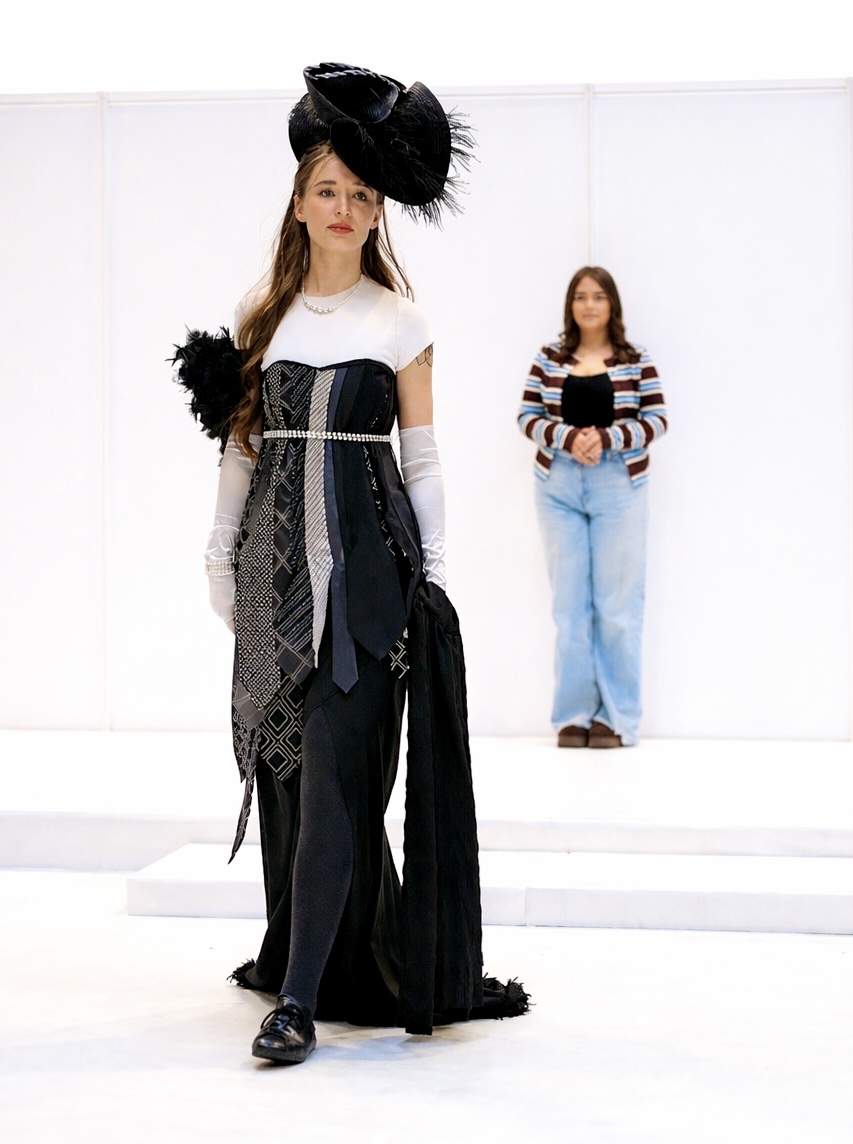 A model wears a black and white outfit - a second person stands behind, looking at them.