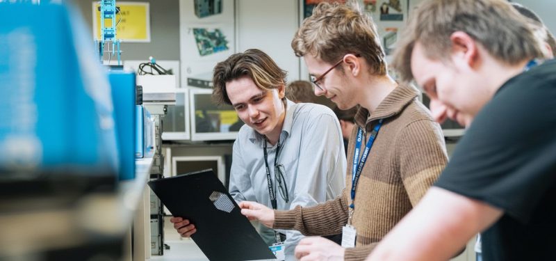 Students in a classroom setting looking at a black clipboard