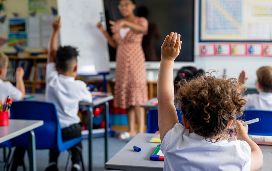 Classroom of young students with hand in the air to answer question