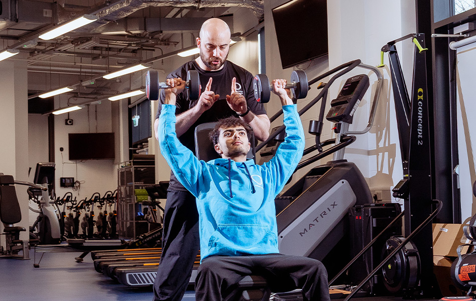 Tutor and male student being shown how to lift weights