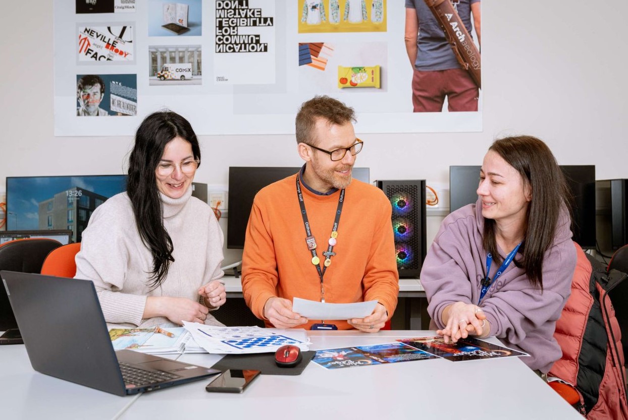 Staff and students sit at a table in a classroom setting.